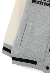 Felpa grigia con tasca frontale, maniche a contrasto in crema e polsini a coste con dettagli neri. Dettaglio logo ricamato incluso.