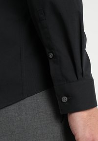 Zwarte blouse met lange mouwen en knoopmanchetten, met een gladde textuur en een slim-fit ontwerp. De stof heeft een matte afwerking.