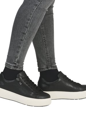 Black leather sneakers with a low profile, featuring a textured surface, white rubber sole, and a side zipper detail. Paired with gray jeans.