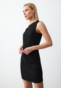 Zwarte mouwloze jurk met een aansluitend ontwerp, textuurstof, gestructureerde lijnen en een zoom tot op de knie. Minimalistische stijl zonder versieringen.