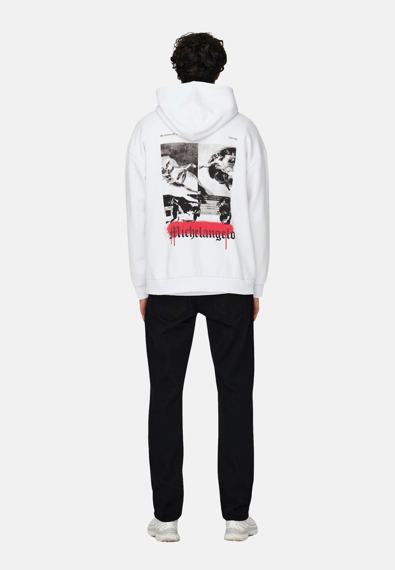 Sudadera blanca con estampados gráficos negros en la parte posterior, que presenta detalles artísticos y la palabra "Michelangelo" en rojo. Lleva puestos pantalones negros.