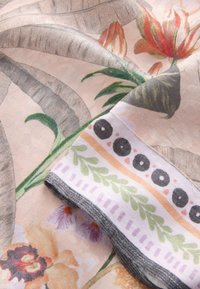 Tissu doux avec des motifs floraux tropicaux aux couleurs atténuées et un bord plié présentant des dessins géométriques et de feuilles.