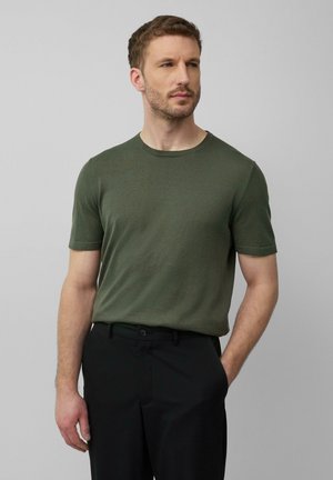 T-shirt vert olive avec un col rond et des manches courtes, fabriqué dans un tissu texturé. Associé à un pantalon noir pour un look neutre.