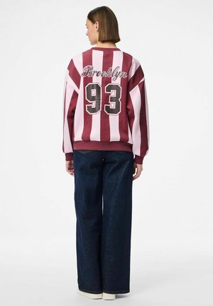 Bordeaux- und rosa gestreifter Sweatshirt mit "Brooklyn" und der Nummer "93" auf dem Rücken, kombiniert mit weit geschnittenen Jeans.