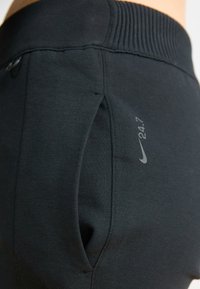 Svarte treningsbukser med ribbestrikket midjebånd, sidelommer og reflekterende Nike-merke. Laget av mykt, elastisk materiale.