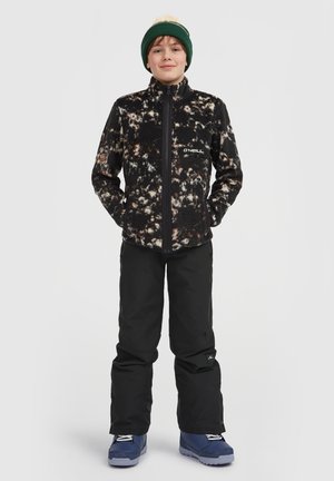 Black fleece jacket with a multi-color abstract pattern, zippered front, and logo detail, paired with black snow pants and blue boots.