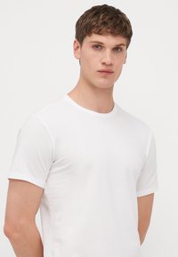 T-shirt blanc à manches courtes avec un col ras du cou, fabriqué en tissu doux, au design ajusté, ne présentant aucun logo ou motif visible.