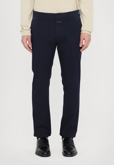Marineblauwe op maat gemaakte broek van soepel materiaal, met een platte voorkant, riemlussen en een rits. Draag het met zwarte schoenen en een lichte bovenkant.