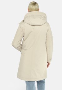 Beige gewatteerde jas met een hoge kraag en een capuchon. Glad materiaal, middellange snit en knoopaccenten op de mouwen.