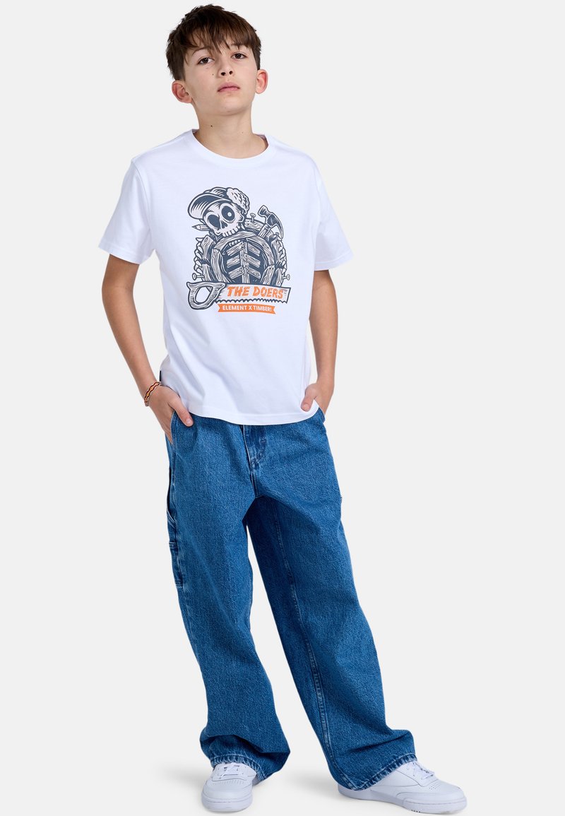 Weißes Baumwoll-T-Shirt mit einem grafischen Design eines Schädels und Werkzeugen, kombiniert mit lockeren blauen Jeans und weißen Turnschuhen.
