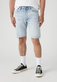 Shorts din denim bleu deschis cu o croială relaxată, cinci buzunare și margine brută. Asortați cu adidași din pânză negri și sosete albe până la gleznă.