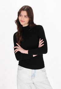 Schwarzer gerippter Pullover mit hohem Kragen und langen Ärmeln, kombiniert mit hellblauen lässigen Jeans. Glattes Material, taillierte Passform.