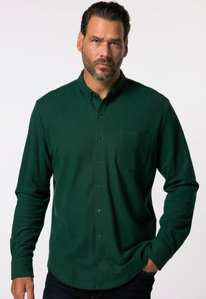 Camisa de botón de manga larga en verde oscuro con un bolsillo en el pecho, hecha de una tela texturizada, presenta un cuello clásico y un dobladillo redondeado.