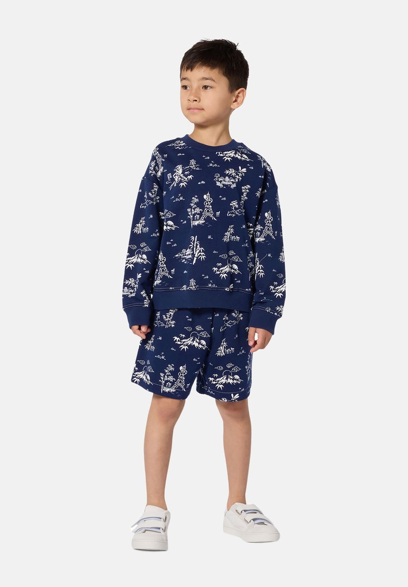 Ensemble sweat-shirt et short bleu marine à motifs avec imprimés blancs sur le thème de la nature ; tissu confortable et coupe décontractée ; associé à des chaussures blanches.