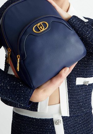 Zaino in pelle blu navy con parte superiore arrotondata, hardware dorato e doppie chiusure a zip. Presenta una superficie testurizzata e un accento con logo distintivo.