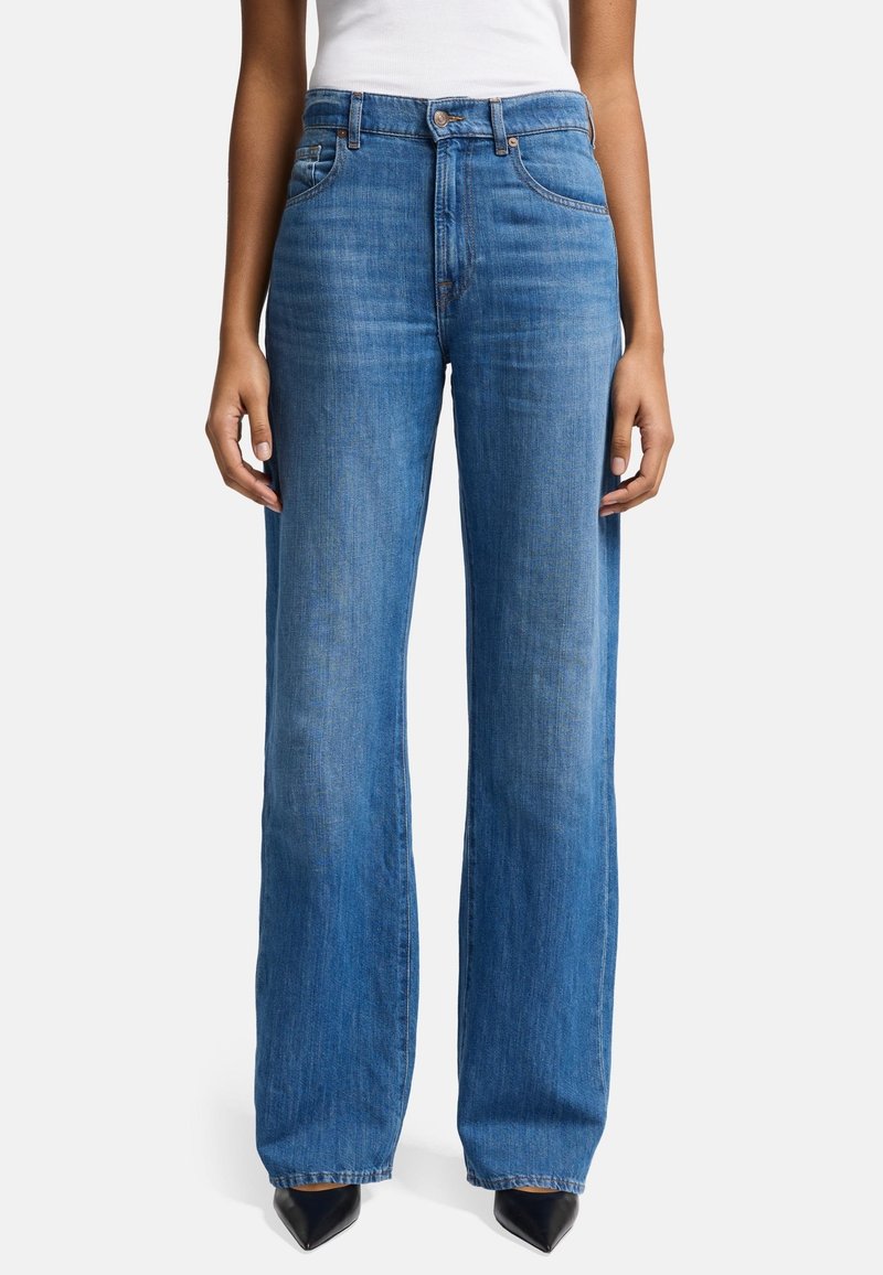 Wijde blauwe denim jeans met een middelhoge taille, subtiele stiksels en uitlopende zoom. Gecombineerd met puntige zwarte hakken voor contrast.