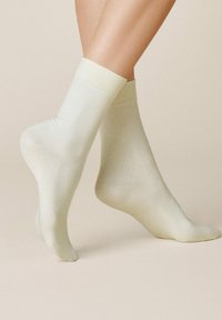 Hellgelbe Knöchelsocken mit glatter Textur und elastischen Bündchen, die eine taillierte Form und ein minimalistisches Design zeigen.
