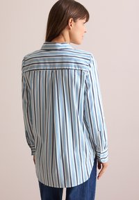Light blue striped shirt with long sleeves, featuring a collar, button cuffs, and a straight back yoke with pleating detail.
