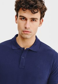 Granatowa koszulka polo wykonana z bawełny, z klasycznym kołnierzykiem, dwoma guzikami z przodu oraz subtelnym haftem logo na piersi.