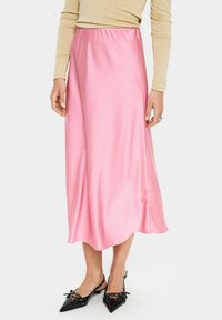 Roze satijnen midi-jurk met een gladde textuur en elastische tailleband, gecombineerd met zwarte schoenen met een spitse neus en decoratieve accenten.