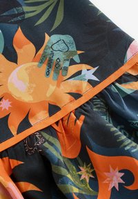 Színes anyag absztrakt nap-, virág- és kézmintákkal narancssárga, zöld és kék árnyalatokban. Redős szegély narancssárga díszítéssel.