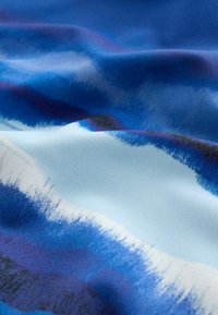 Tissu bleu et blanc avec des motifs abstraits ondulés et des plis doux créant une apparence texturée et fluide.