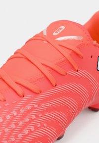 Scarpino da calcio corallo brillante con tomaia testurizzata, strisce bianche di accento e lacci sottili. Tacchetti in gomma per trazione.