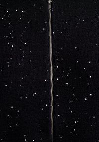 Černý zip-up oděv, který má rozptýlené stříbrné flitry a texturovanou látku. Výrazný středový zip dodává na funkčnosti.