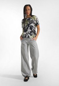 Pantalones deportivos grises holgados con bolsillos laterales, combinados con una camiseta negra de manga corta con estampado floral. La tela parece suave y cómoda.