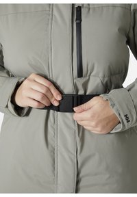 Hellgraue isolierte Jacke mit einem schwarzen Reißverschluss und einem Gürtel. Sie verfügt über einen gerippten Bündchen und ein Logodetail am Ärmel, entworfen für Wärme und Komfort.
