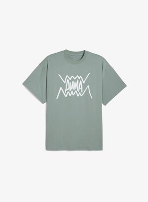 Tricou verde din bumbac, cu manșete scurte, având un design grafic zimțat alb cu cuvântul "PUMA" centrat pe față.