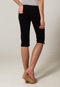 Jeans capri noirs avec une coupe slim, présentant deux poches arrière et des détails de couture subtils. Le tissu est lisse et extensible.