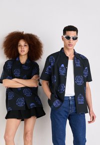 Zwarte shirts met blauwe grafische patronen, met korte mouwen, een kraagontwerp en een relaxte pasvorm, gecombineerd met denim en een zwarte rok.