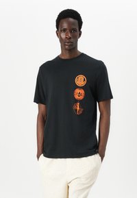 Tricou negru din bumbac, cu modele grafice portocalii aranjate circular pe piept. Mâneci scurte, guler rotund.