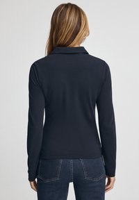 Marineblaue Polohemd mit langen Ärmeln, Kragen, glatter Textur und figurbetontem Design. Die Rückansicht zeigt Nahtdetails und einen geraden Saum.