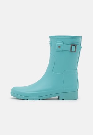 Botte de pluie en caoutchouc turquoise avec un bout arrondi, accent de boucle réglable, bord supérieur texturé et semelle plate.