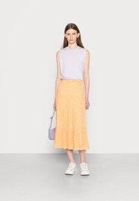 Top lilás sem mangas combinado com uma saia amarela de flores em camadas. Ténis brancos e uma pequena mala cruzada roxa completam o visual.