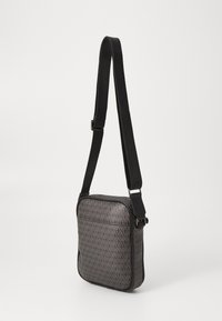 Petit sac rectangulaire bandoulière avec une sangle noire réglable et un motif géométrique gris sur le devant et les côtés.