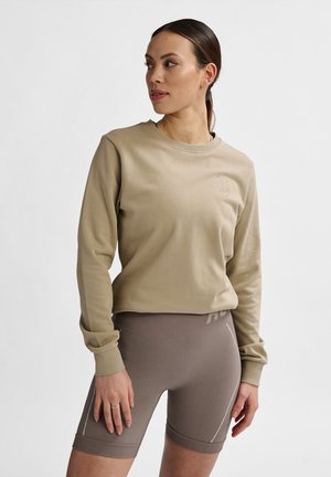 Beige lange mouwen top en bijpassende geribbelde shorts, beide gemaakt van zacht materiaal. De top heeft een subtiele logo en een relaxte pasvorm. De shorts hebben een brede tailleband.