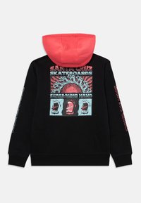 Hoodie noir avec une capuche bordée de rouge. Le dos présente des graphiques colorés sérigraphiés de visages et de texte, avec des manches longues affichant des designs supplémentaires.