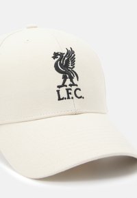 Casquette de baseball couleur crème en tissu avec un logo Liverpool FC brodé en noir, comportant un oiseau et le texte "L.F.C." sur le devant.