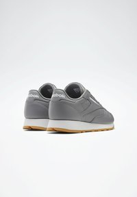 Pelēki sporta apavi ar gludu ādas virsu, baltu vidusdaļu un gumijas zoli, ar detalizētu šuvumu un logotipa akcentiem.