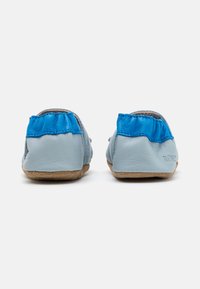 Pantuflas de cuero suave azul con un detalle recogido azul en el talón y una suela de ante color tostado, que presentan un acabado texturizado.