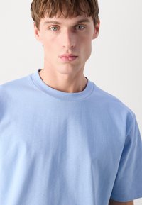 Ανοιχτό μπλε βαμβακερό μπλουζάκι με στρογγυλή λαιμόκοψη, κοντά μανίκια και απαλή υφή, που προβάλλει ένα απλό και καθαρό σχέδιο.