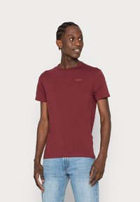 Bordeaux kortere mouwen t-shirt gemaakt van zacht katoen. Heeft een klassieke ronde halslijn en een subtiele logo op de borst. Gecombineerd met lichtblauwe spijkerbroek.