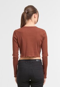 Smeđi rebrasti dugih rukava crop top s sirovim rubom, uparen s crnim uskim trapericama koje imaju stražnje džepove i kožnu oznaku.