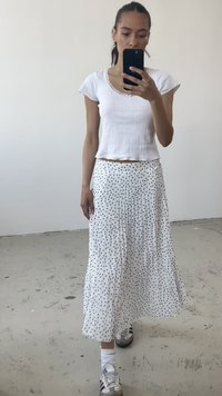Hvid kortærmet top med ribbet tekstur, parret med en hvid plisseret nederdel med sorte polka dots, båret med grå og hvide sneakers.