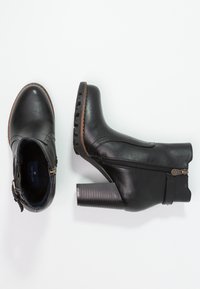 Bottines noires en matériau synthétique. Elles disposent d'une fermeture éclair sur le côté, d'un talon texturé et d'une semelle contrastante marron. Design à bout rond.