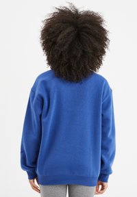 Sudadera azul con un corte relajado, puños acanalados y tejido suave. Presenta un cuello redondo y una textura lisa. Mostrada desde la parte trasera.