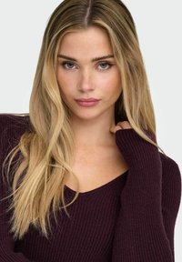 Maglione color amaranto a costine con scollo a V e maniche lunghe. La trama sembra morbida e leggermente elastica, adatta per un abbigliamento casual.